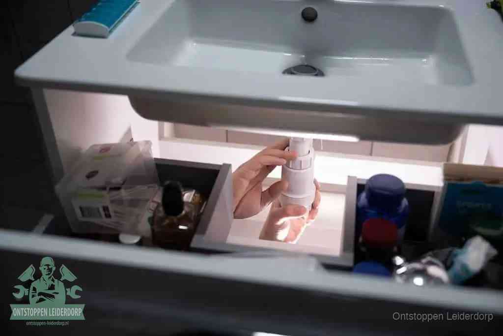 Een pompfles met zeep boven een wastafel, de heet water en afwasmiddel-methode om een vetprop in de afvoer los te maken in Leiderdorp