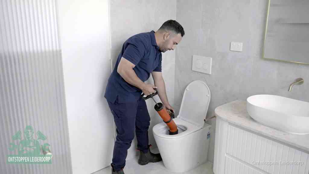 Een monteur buigt over een wandcloset en duwt met de hand een persluchtontstopper in de toiletpot om de verstopping handmatig los te maken in Leiderdorp