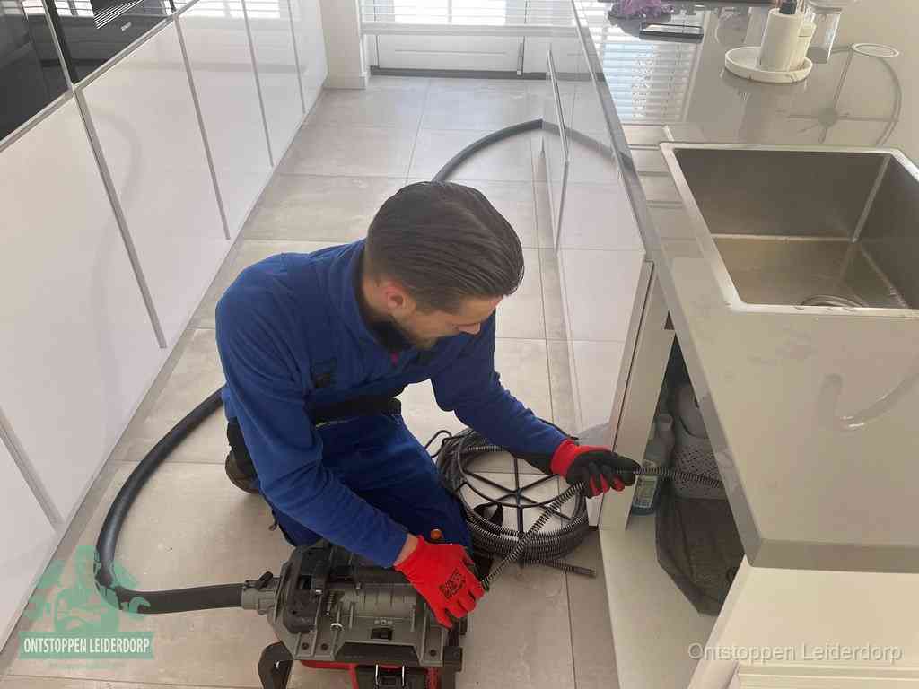 Een monteur ontstopt de keukenafvoer onder de spoelbak met een elektrische veermachine in Leiderdorp