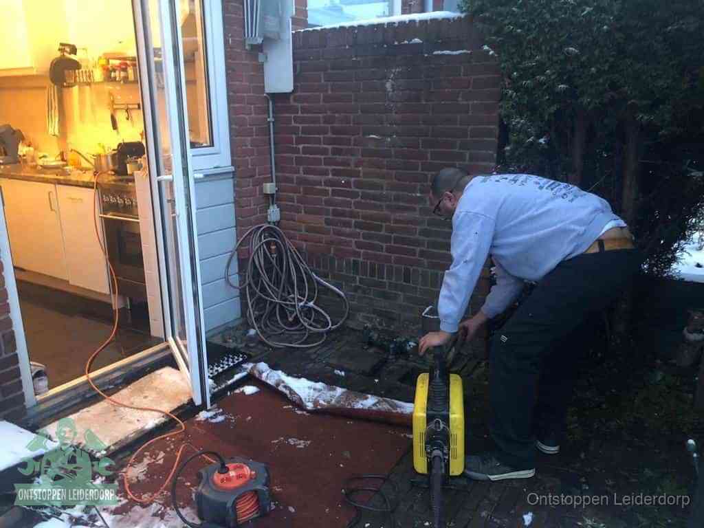 Een monteur werkt buiten bij een open riool-/grondput met een elektrische ontstoppingsmachine om een verborgen afvoerprobleem op te sporen in Leiderdorp