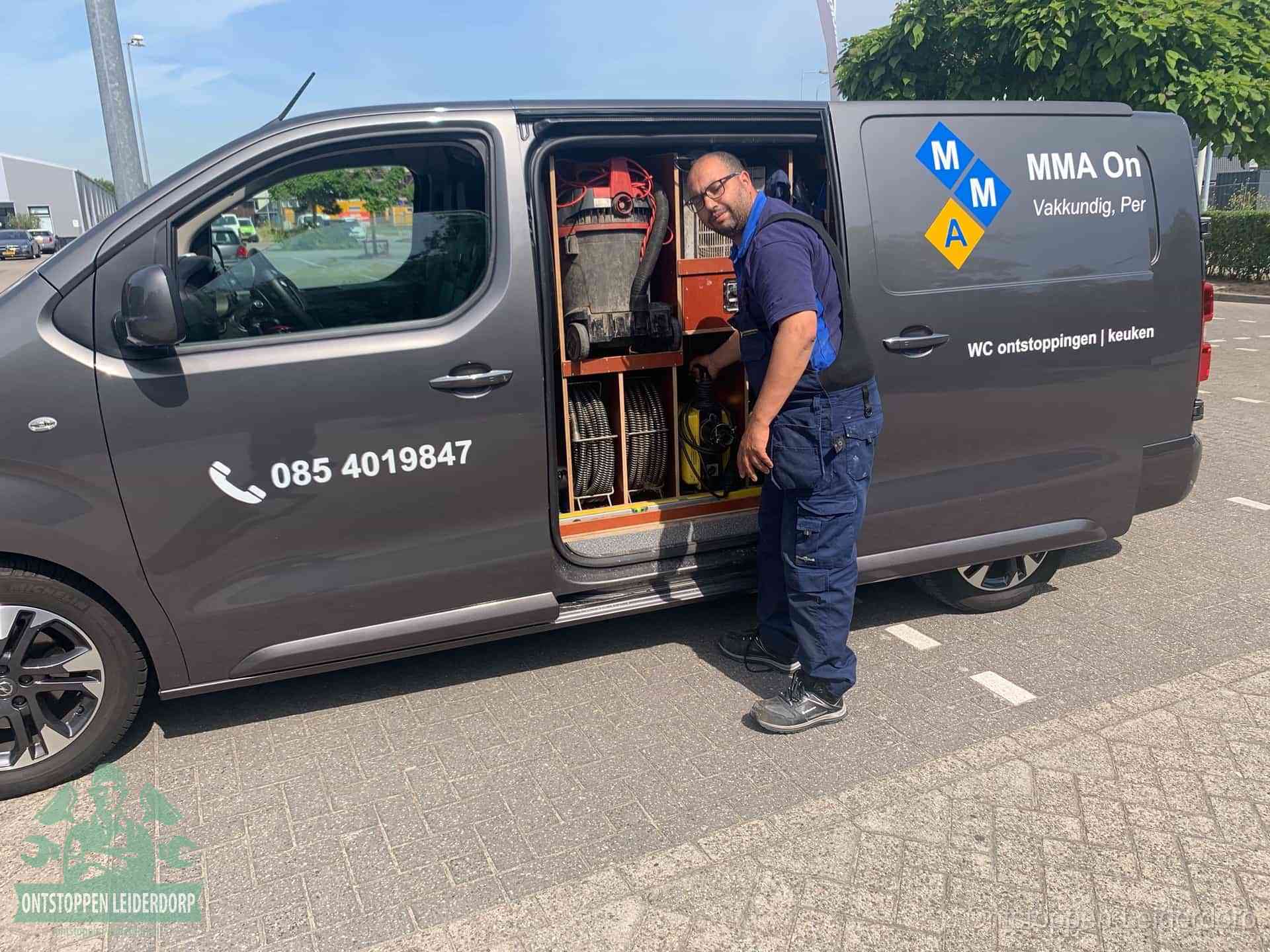 Een monteur bij de open schuifdeur van zijn bedrijfsbus op een parkeerplaats, klaar om de oorzaak van terugkerende afvoerverstoppingen aan te pakken in Leiderdorp