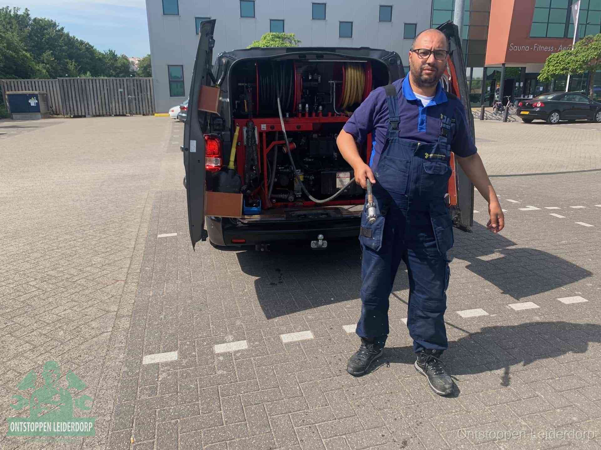 Een monteur bij zijn bestelbus met een hogedruk- en rioolreinigingsunit, klaar om de oorzaak van terugkerende wc-verstoppingen aan te pakken in Leiderdorp