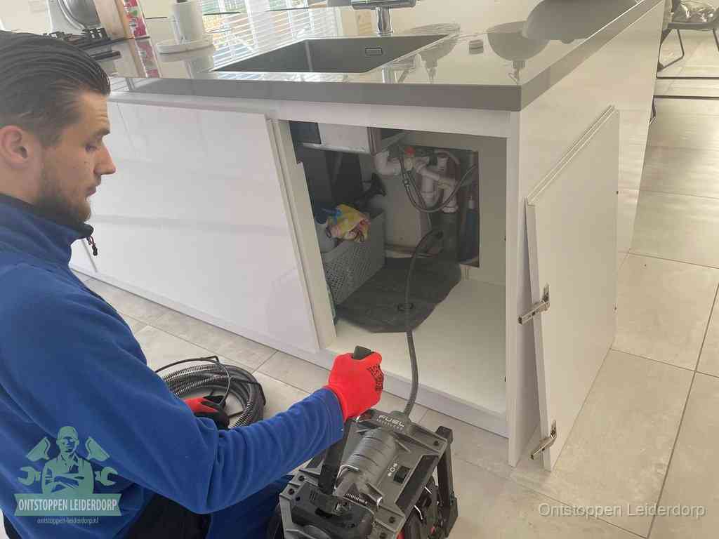 Monteur ontstopt met een veermachine een verstopte afvoer onder de gootsteen in Leiderdorp