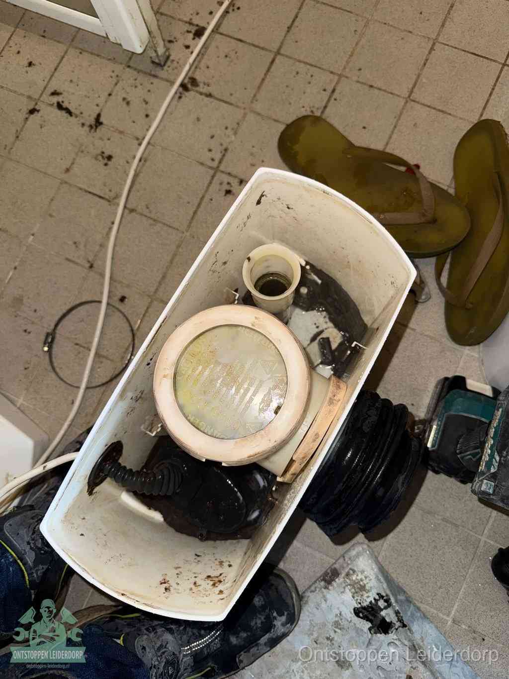 Een gedemonteerde toiletpot op de vloer met ontstoppingsveer en gereedschap ernaast, het verwijderen van een vastzittend voorwerp uit de wc in Leiderdorp