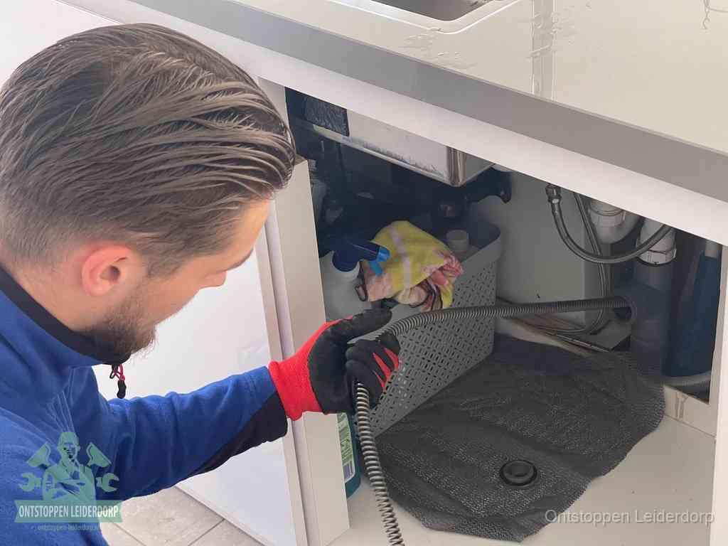 Een monteur voert een flexibele ontstoppingsveer in de afvoer om een verstopping voorbij de bocht van het toilet te bereiken in Leiderdorp